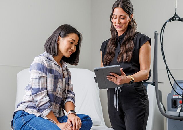A woman wearing a plaid shirt speaks with a Milan Laser Provider in an image for a blog titled Laser Hair Removal Consultation Questions.