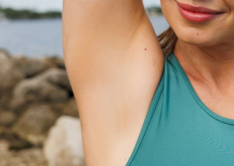Close up of a person raising their arm after getting transgender laser hair removal and grinning with rocks in the background