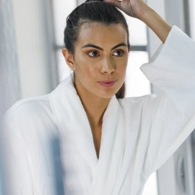 Woman looking confident after getting facial laser hair removal looking in the mirror