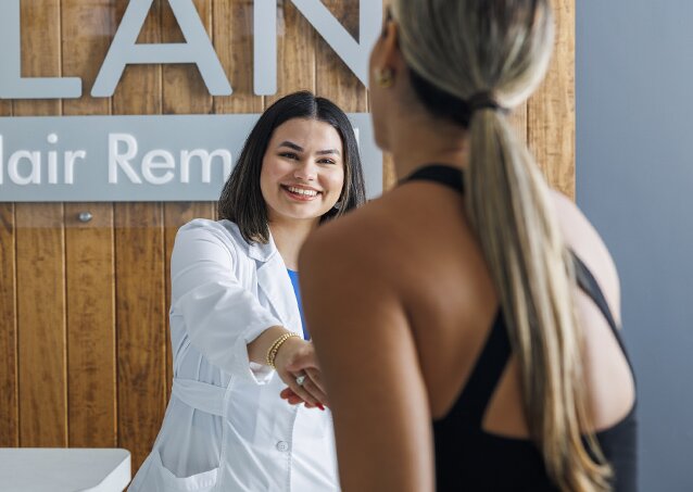 Woman in a black tank top in a Milan clinic wondering if she can get laser hair removal with white hair and shaking a clinic manager's hand