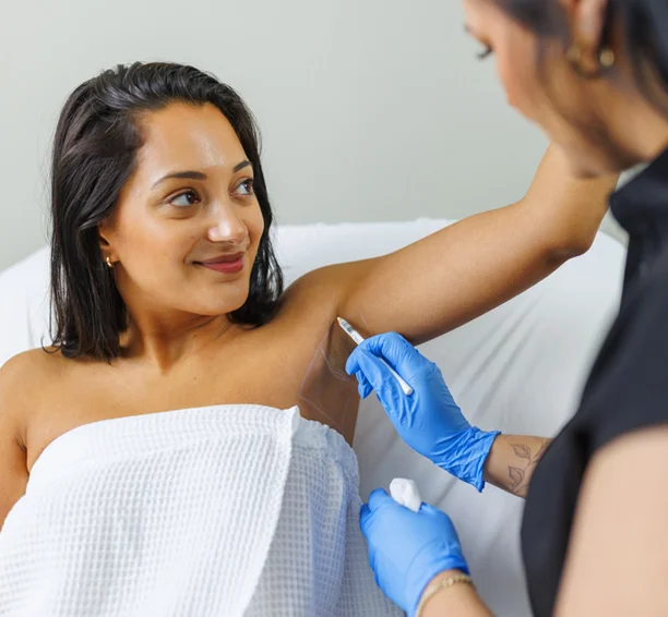 Woman raising her arm above her head and looking left as a Milan clinic staff member draws a grid on her underarm