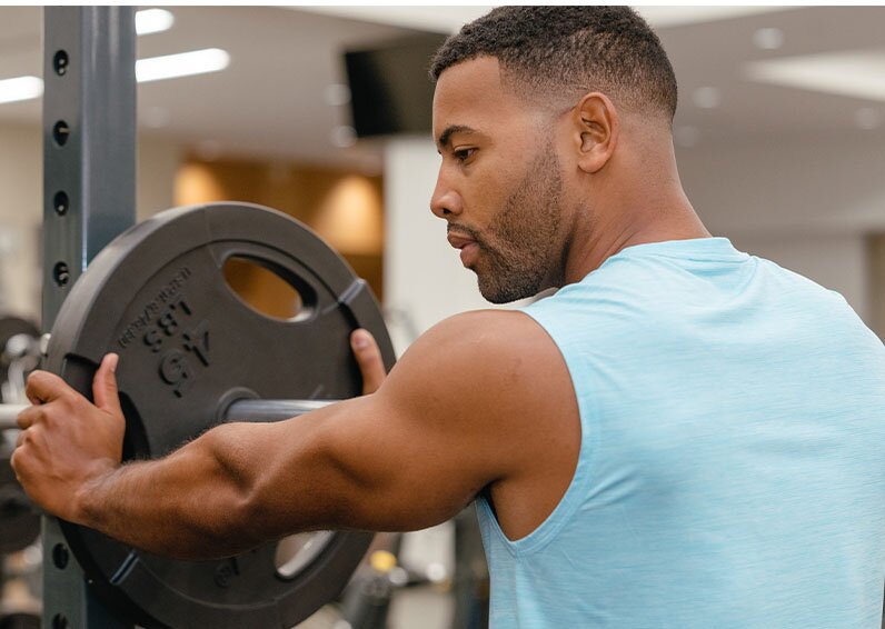 Man grabbing weights in a blue shirt and looking left after getting neck laser hair removal