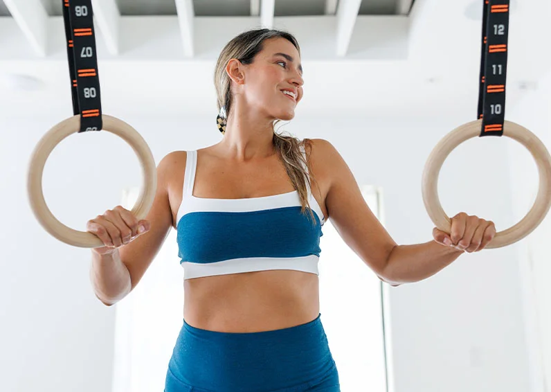 Happy woman holding rings in a gym, brimming with confidence because she got full body laser hair removal