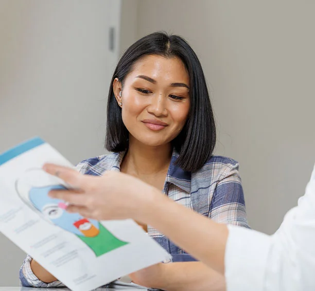 Woman in a blue button-up shirt grinning with a medical professional in a consultation for eyebrow laser hair removal