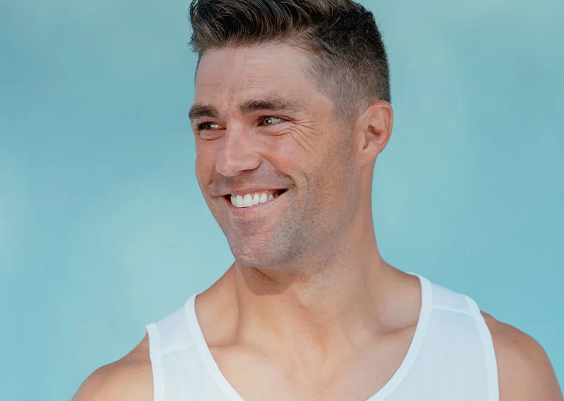 Smiling man looking to his left wearing a white tank top