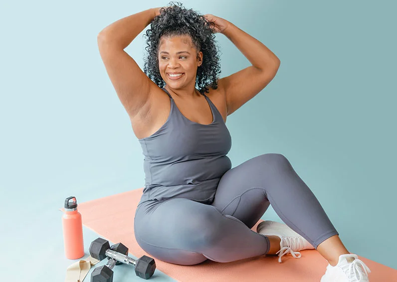 Woman in a grey workout set holding her arms above her head after working out, with extreme confidence because she just got chin laser hair removal