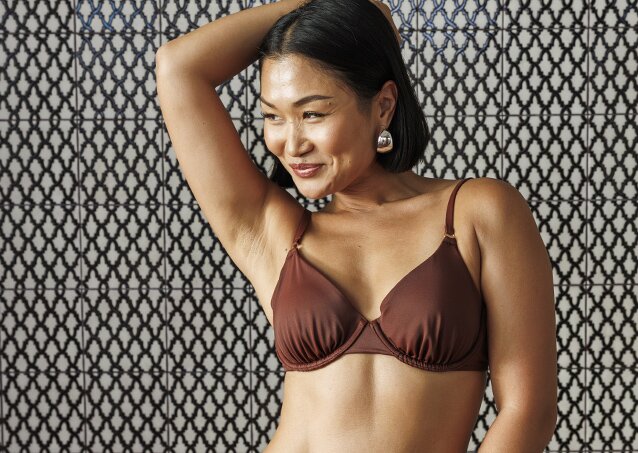 Pretty Asian woman in a brown bikini smiling and looking right as an image for a piece titled Laser Hair Removal for Folliculitis