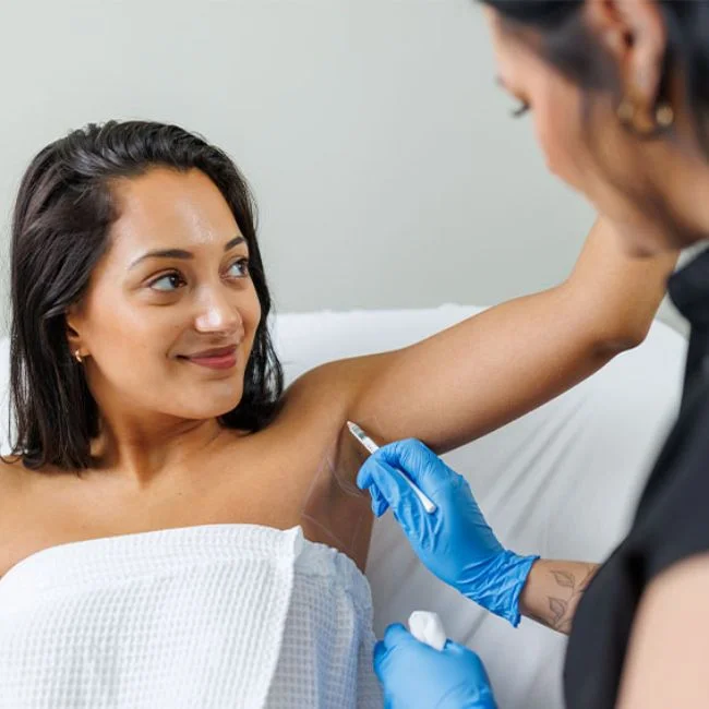 Woman in a white treatment robe holding her arm up and getting underarm laser hair removal