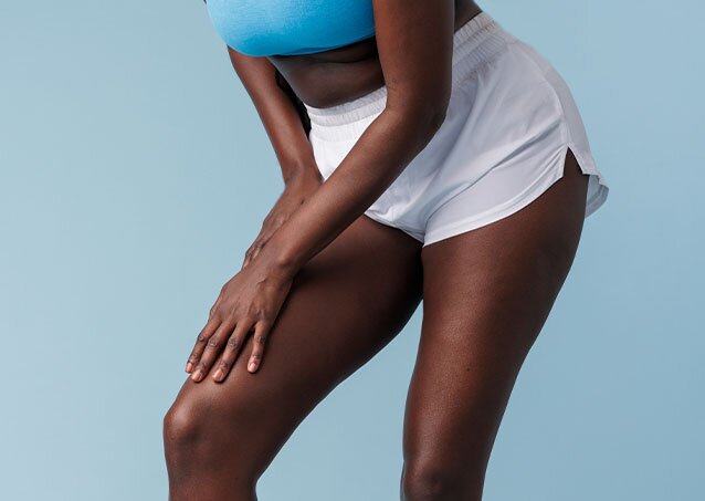 Woman in a blue sports bra and white athletic shorts holding her leg as an image for a blog post on side effects of hair removal cream on private parts