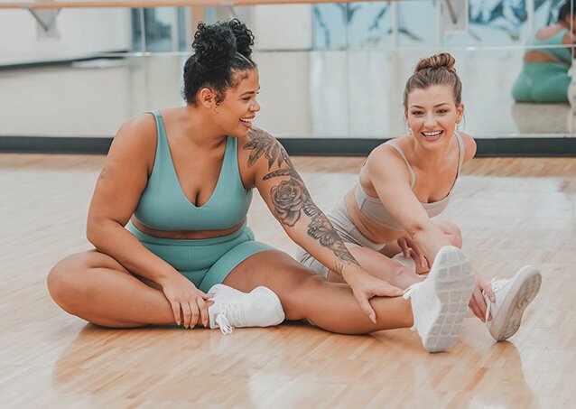 Woman in a pink bikini sitting on a yellow and white-striped towel brimming with confidence because she learned the answer to why does my leg hair grow so fast?