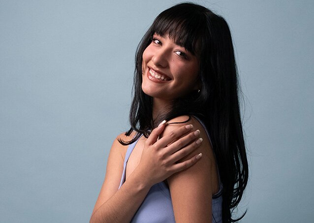 A woman wearing a purple top feels the smooth skin on her arm in an image for a blog titled The Difference Between IPL and Laser Hair Removal.