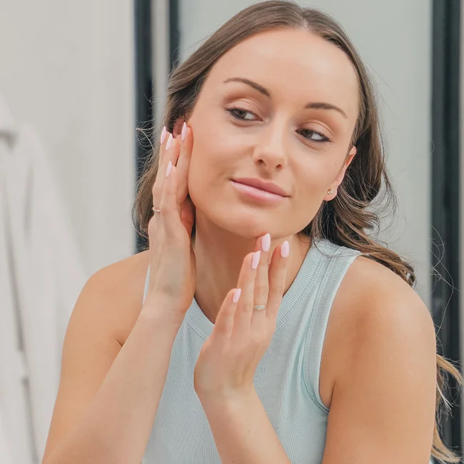 Woman in a blue workout top looking in the mirror and admiring her smooth skin as a result of face laser hair removal