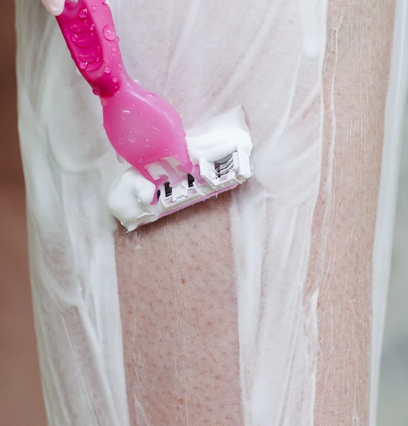 Person shaving their legs with a pink razor after learning how to prepare for laser hair removal