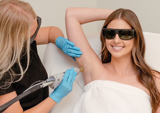Woman holding her arm above her head and smiling while getting treated for a piece on laser hair removal facts