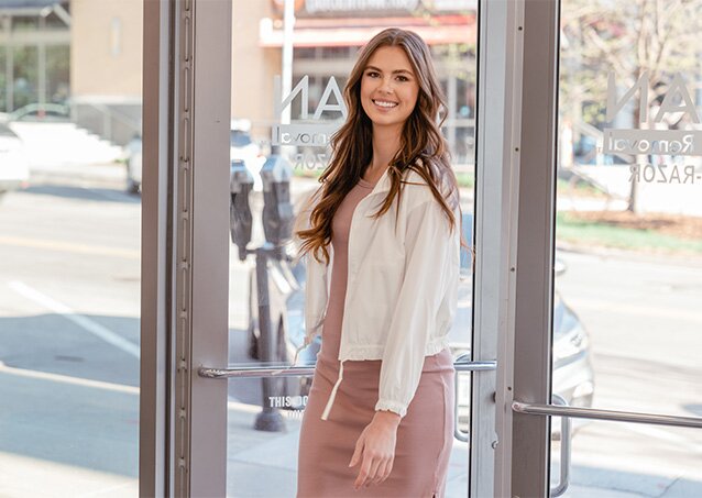 A woman in purple clothing and a white coat enters a Milan Laser clinic in an image for a blog titled How To Get The Best Results From Laser Hair Removal.