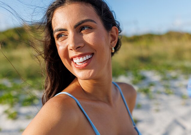 Woman with brown hair and white teeth smiling and looking right as an image for a blog post titled is waxing your face bad