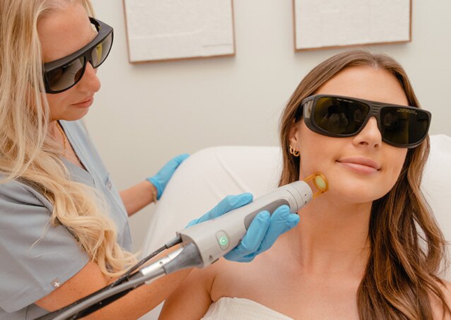 A woman wrapped in a white towel and wearing protective eyewear receives laser hair removal on her chin from a Milan Laser Provider in an image for a blog titled Customization and Calibration Features For Optimal Hair Removal Treatments.