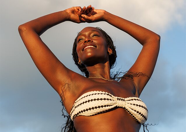A woman wearing a black and white bikini enjoys some time basking in the sunlight in an image for a blog titled Laser Hair Removal Side Effects: What’s Normal, What’s Not, and When To Call.