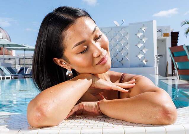 A woman enjoys some time sunbathing in the pool and beaming with confidence because she knows how to stop facial hair growth due to PCOS.