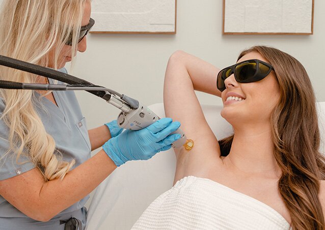 A woman wrapped in a white towel receives laser hair removal on her underarm from a Milan Provider in an image for a blog titled Can Laser Hair Removal Cause Skin Discoloration?