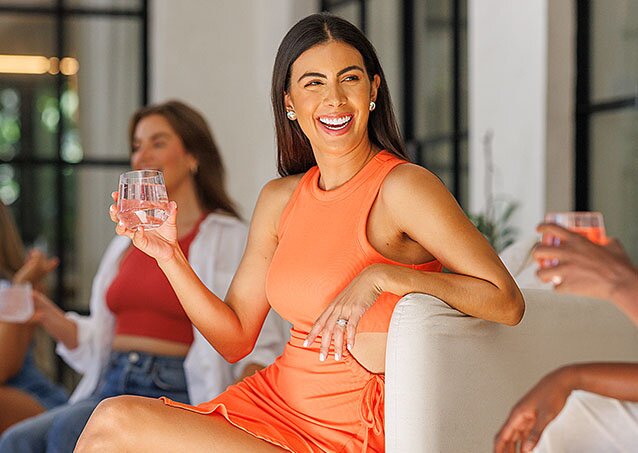 Woman smiling and holding a glass of water excitedly because she learned that she can get laser hair removal with diabetes
