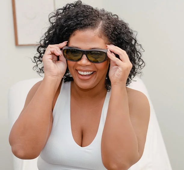 Woman holding black sunglasses up to her face and smiling