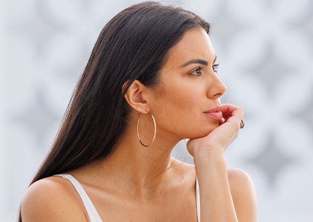 Happy woman holding her hand to her chin after getting laser hair removal on accutane and wearing a white camisole while standing outside