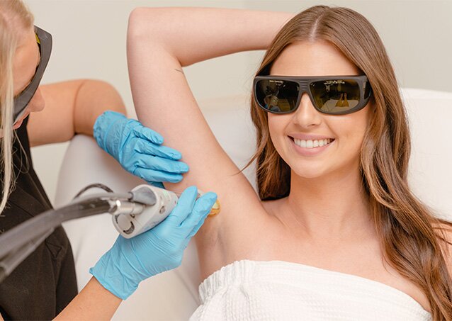 Woman in protective glasses smiling and raising her arm above her head while in a white Milan Laser treatment chair holding her arm above her head as an image for a blog post on Botulinum Toxin and Laser Hair Removal