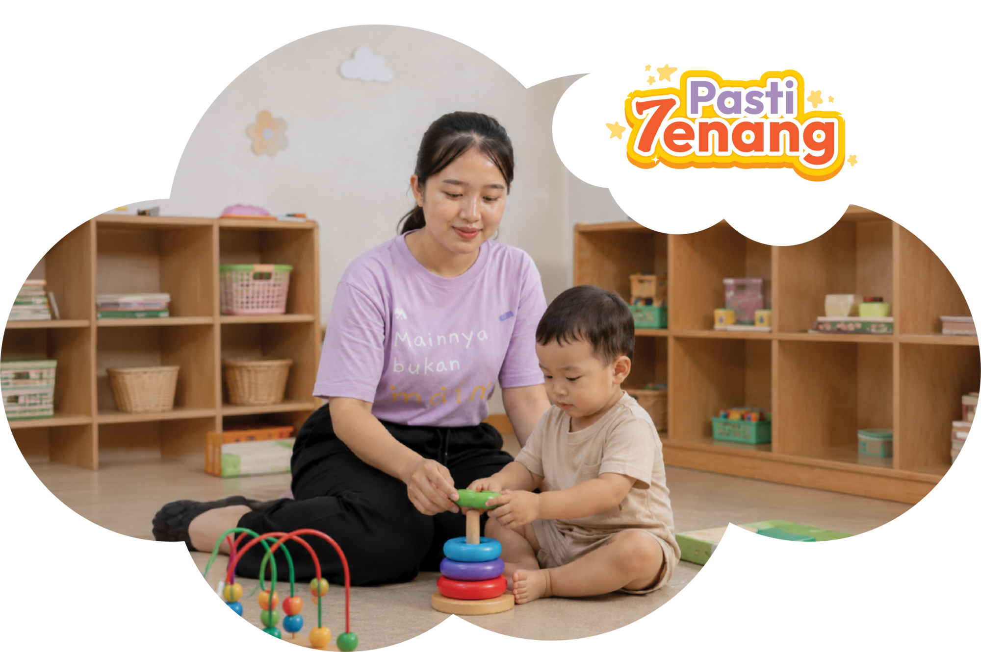 Seorang pengasuh sedang membacakan buku cerita kepada dua balita yang tersenyum di dalam ruang kelas daycare.