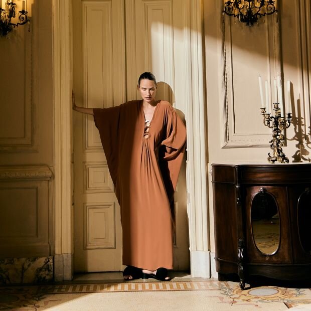 A model wearing brown kaftan with ring accents at the front.