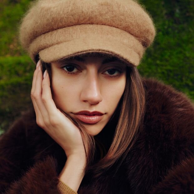 A model wearing a beige wool baker boy cap with a rounded crown and gently curved brim.
