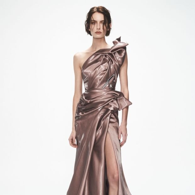 A model wearing a pink metallic one-shoulder gown with structural elements.