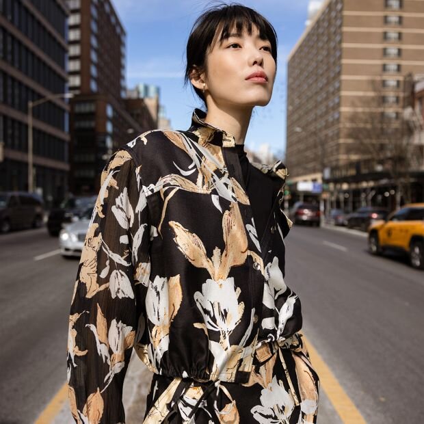 A model wearing a floral print cotton-silk blend shirt jacket featuring a classic button-front silhouette and collar with a flap pocket at the chest and a cinched drawstring waist.
