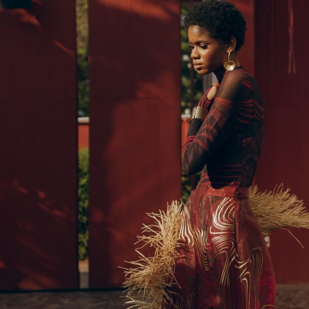 A model wearing a patterned red and black mesh mock neck bodysuit with matching wide leg pants.