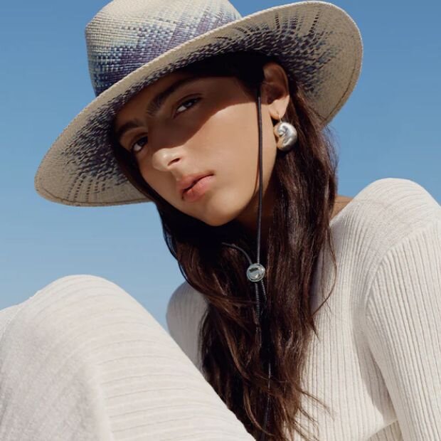 A model wearing a woven straw wide-brim fedora with blue details and a leather chin strap.