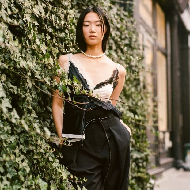 A woman wearing a a satin tank top with contrasting black and white colors with a lace trim and a side drape.