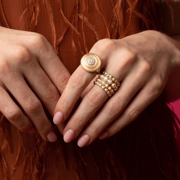 A model wearing 2 gold and diamond rings, one is in a signet style, the other is a band.