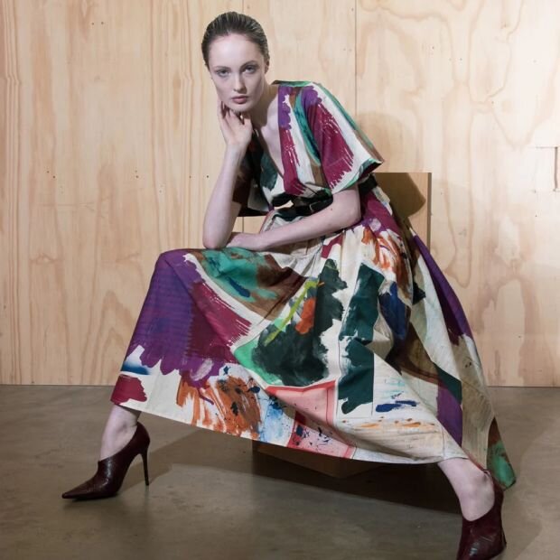 A model wearing a pleated midi dress featuring a colorful abstract print with a belted waist for a fit-and-flare silhouette.