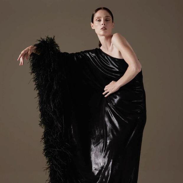 A woman wearing an asymmetric black gown with a feather-trim on one sleeve.