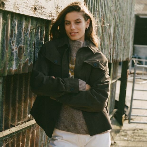 A model wearing an olive green twill overshirt with a button-up collared neckline worn with a grey turtleneck underneath.