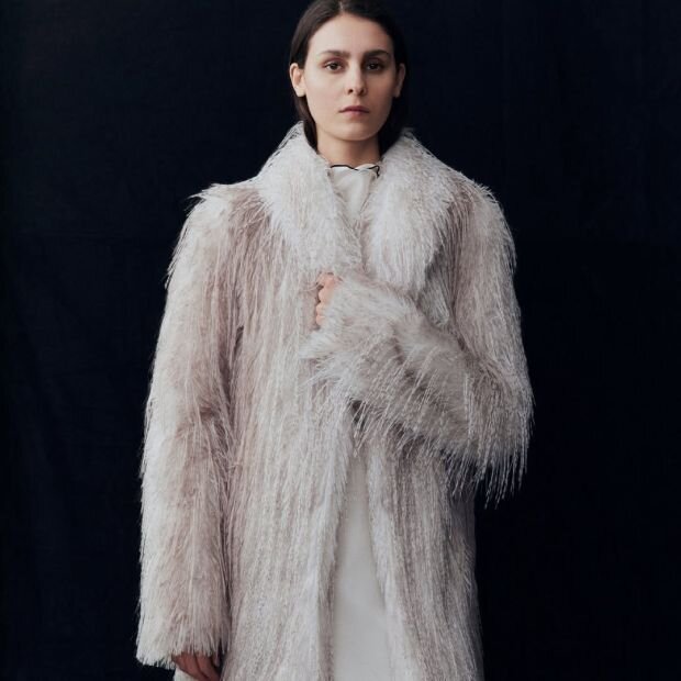 A model wearing an ivory faux fur coat with a shawl collar and an A-line silhouette.