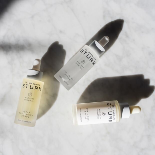 Three bottles of skin care serums against a white marble surface.