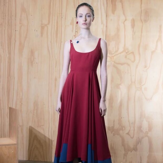 A model wearing a red pleated crepe midi dress with  scooped front and back bodice, featuring a fluid sidetail hemline in royal blue.