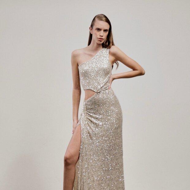 A model wearing a silver sequin gown featuring an asymmetric shape with its single-shoulder neckline and cutout side detail.