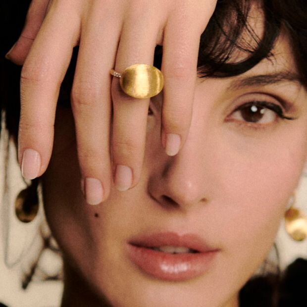 A model wearing a diamond & 18k gold ring  featuring a hand-engraved textured finish and a collection of sparkling diamonds along the band.