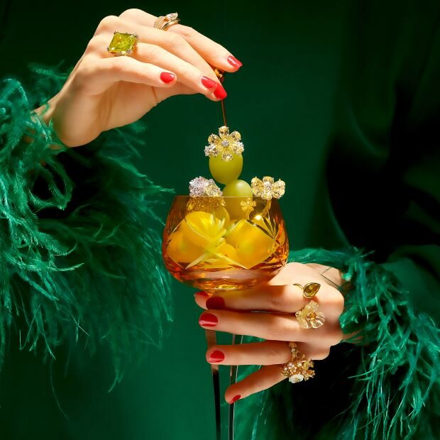 A model wearing multiple statement gem rings holding a glass of grapes embellished in gems.