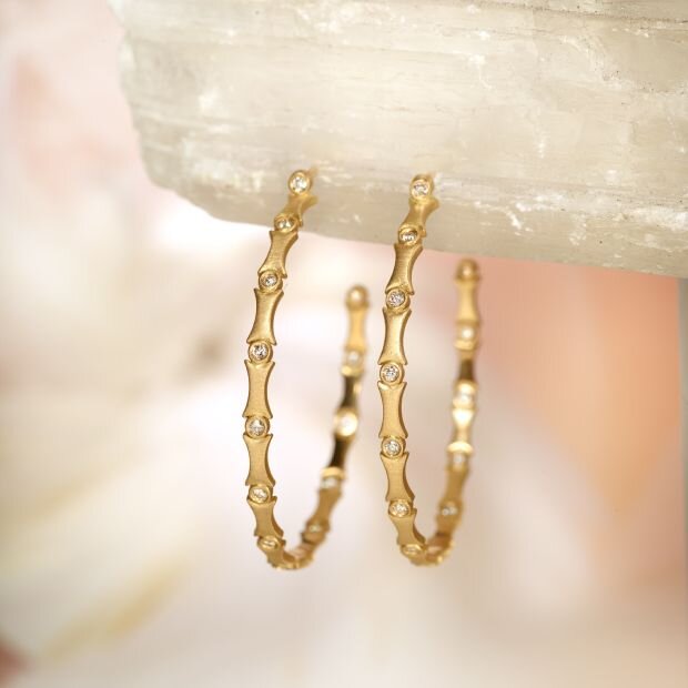 A pair of gold hoops with  an alternating pattern of bamboo-inspired links and bezel-set diamond embellishments.