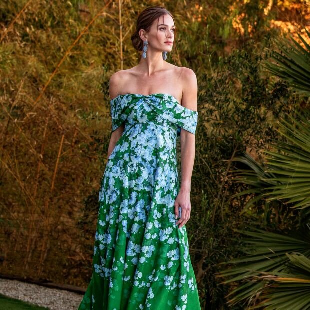 A model wearing an emerald green and light blue floral off-the-shoulder gown.
