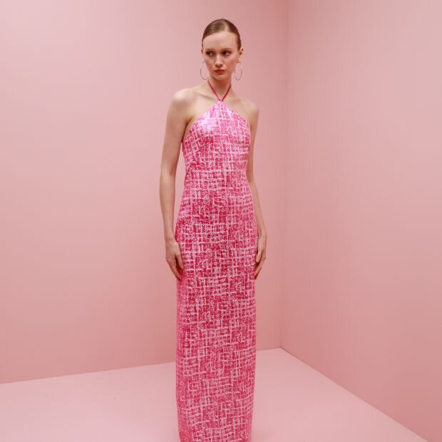 A model wearing a sleek halter dress with a textured pink fabric and a figure-hugging silhouette. 
