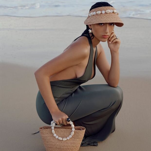 A model wearing a matching raffia hat and handbag featuring resin pebble embellishments.